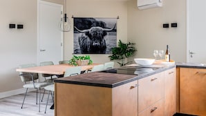 A modern kitchen with a wooden dining table, chairs, a central island, and a large black and white photograph on the wall. - 2 bedroom gorgeous home in Afferden (Afferden)