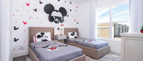 A hotel room with two beds, Mickey Mouse wall decals, a large window, and a view of buildings outside.