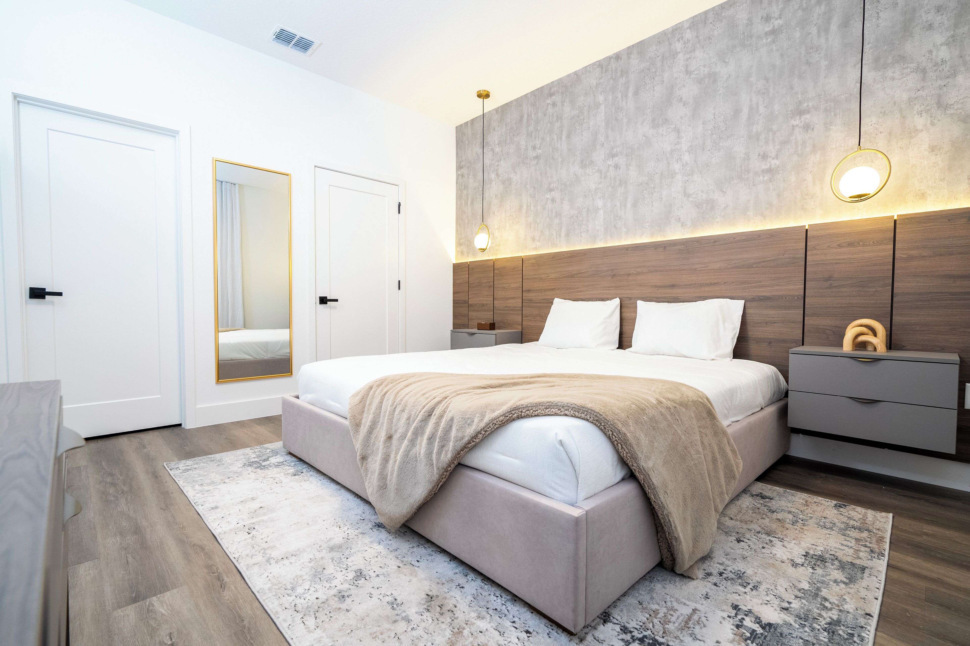 A modern bedroom with a large bed, bedside tables, a wardrobe, and a mirror.