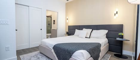 A modern bedroom with a large bed, bedside tables, and a nightstand with a lamp.