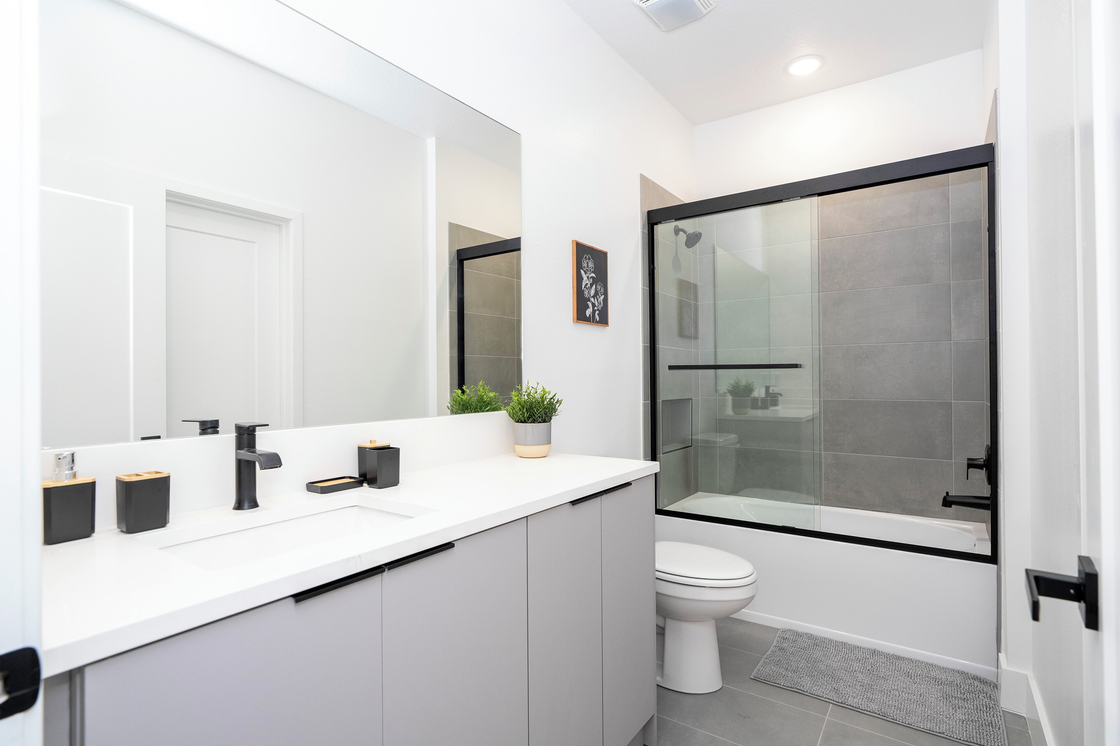 A modern bathroom with a white vanity, a large mirror, a glass shower enclosure, and a toilet.