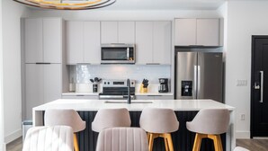 A modern kitchen with white cabinetry, a stainless steel refrigerator, a microwave, and a central island with bar stools. - Doppio Westside (Davenport)