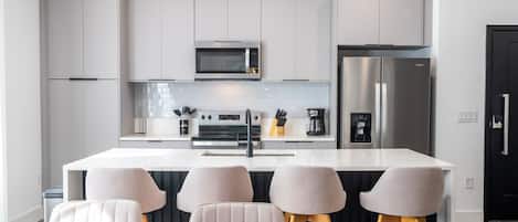 Una cocina moderna con armarios blancos, un refrigerador de acero inoxidable, un microondas y una isla central con taburetes de bar.