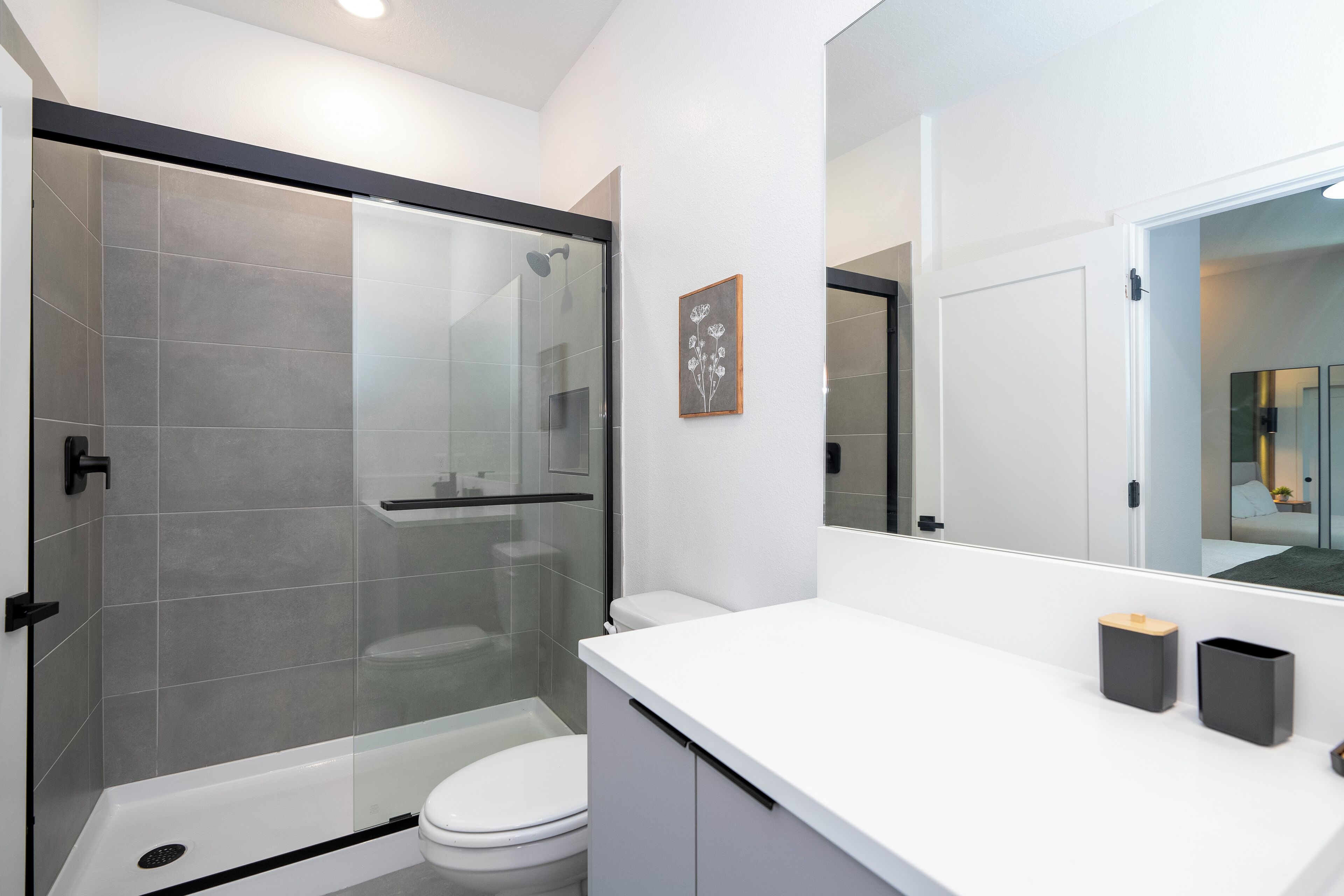 Un baño moderno con ducha de vidrio, inodoro blanco y un espejo grande.