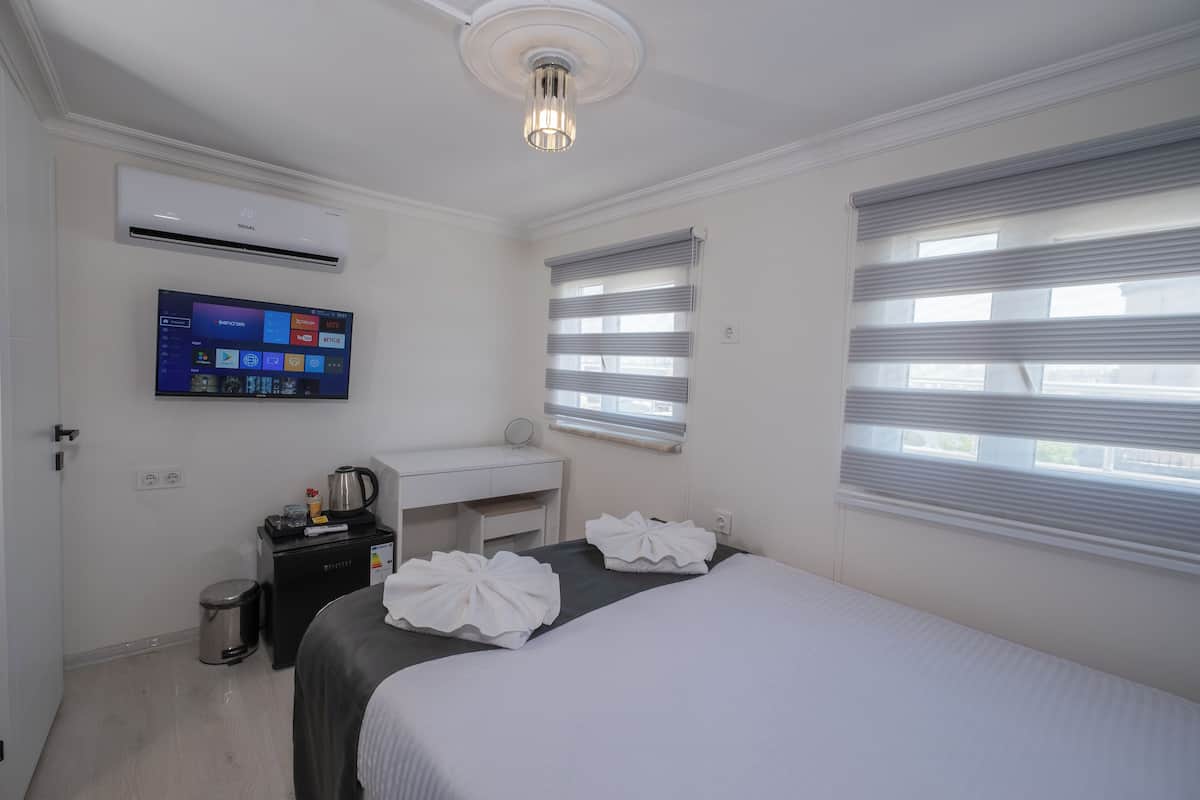 Quarto de hotel com cama, escrivaninha, televisão e janela com persianas.