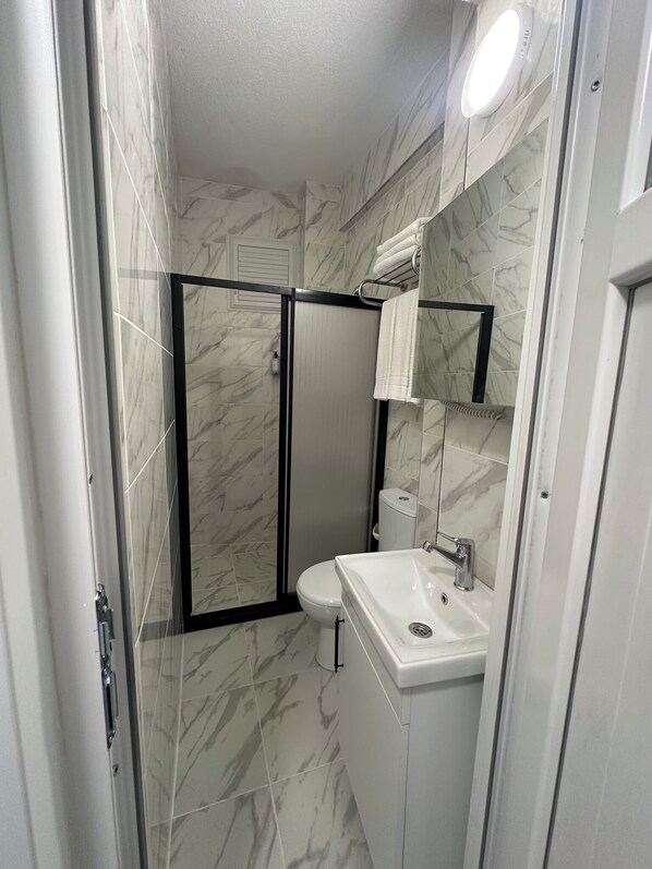 Une salle de bain équipée d’une douche, de toilettes et d’un lavabo, le tout avec des murs recouverts de carreaux de marbre.