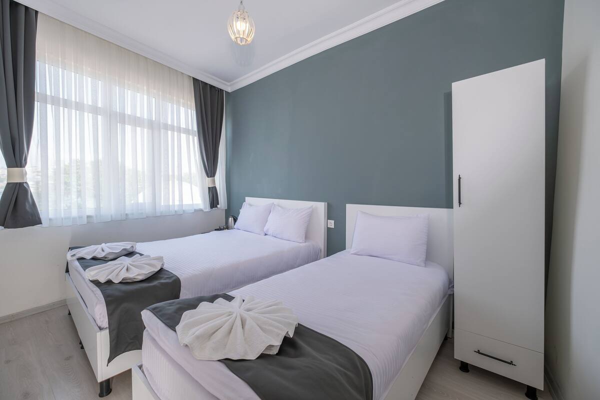 Quarto de hotel com duas camas, um guarda-roupa e uma janela com cortinas.