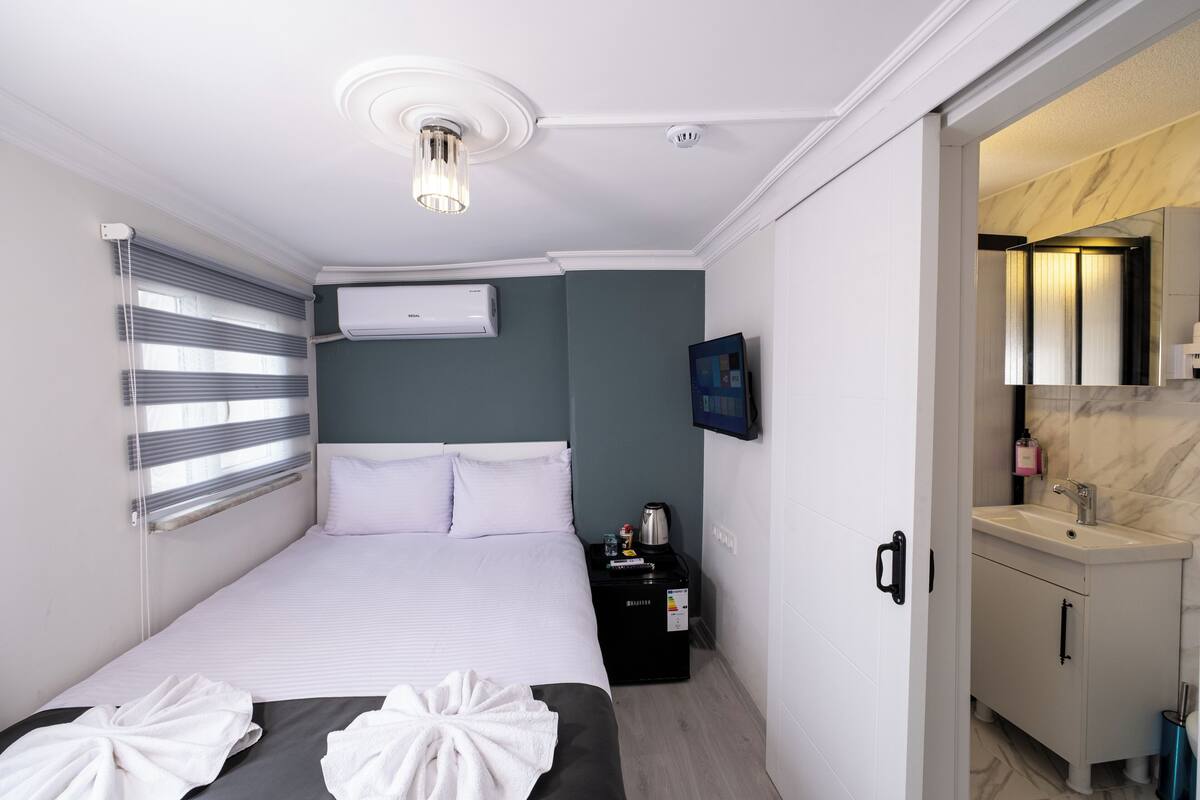 Quarto de hotel com cama, mesa de cabeceira, aparelho de ar condicionado e banheiro com pia e espelho.