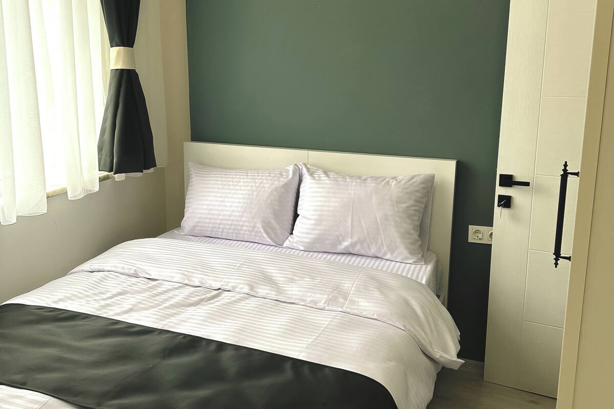 Cama bem arrumada com roupa de cama branca e preta, parede verde e porta branca.