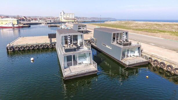 A floating houseboat docked at a marina with a clear view of the sea.