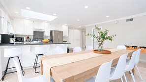 A modern kitchen with white cabinets, a central island, and a dining area with a wooden table and white chairs. - Modern Spacious 5BR Retreat - Games & Large Yard (San Jose)