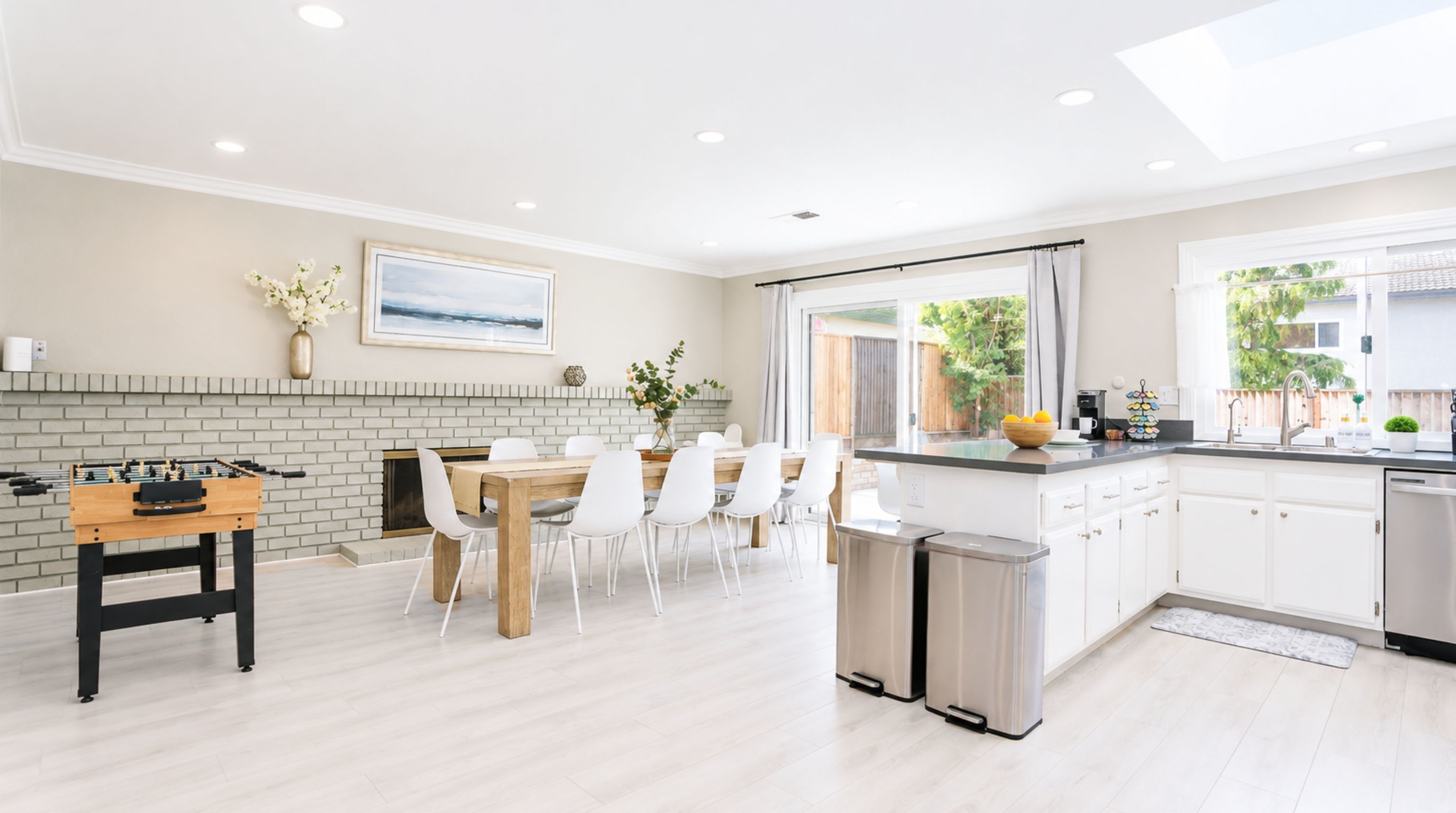 A modern kitchen with a dining area, a foosball table, and a large window offering a view of the outdoors.