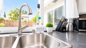A kitchen with a stainless steel sink, a faucet, a potted plant, and kitchen utensils.