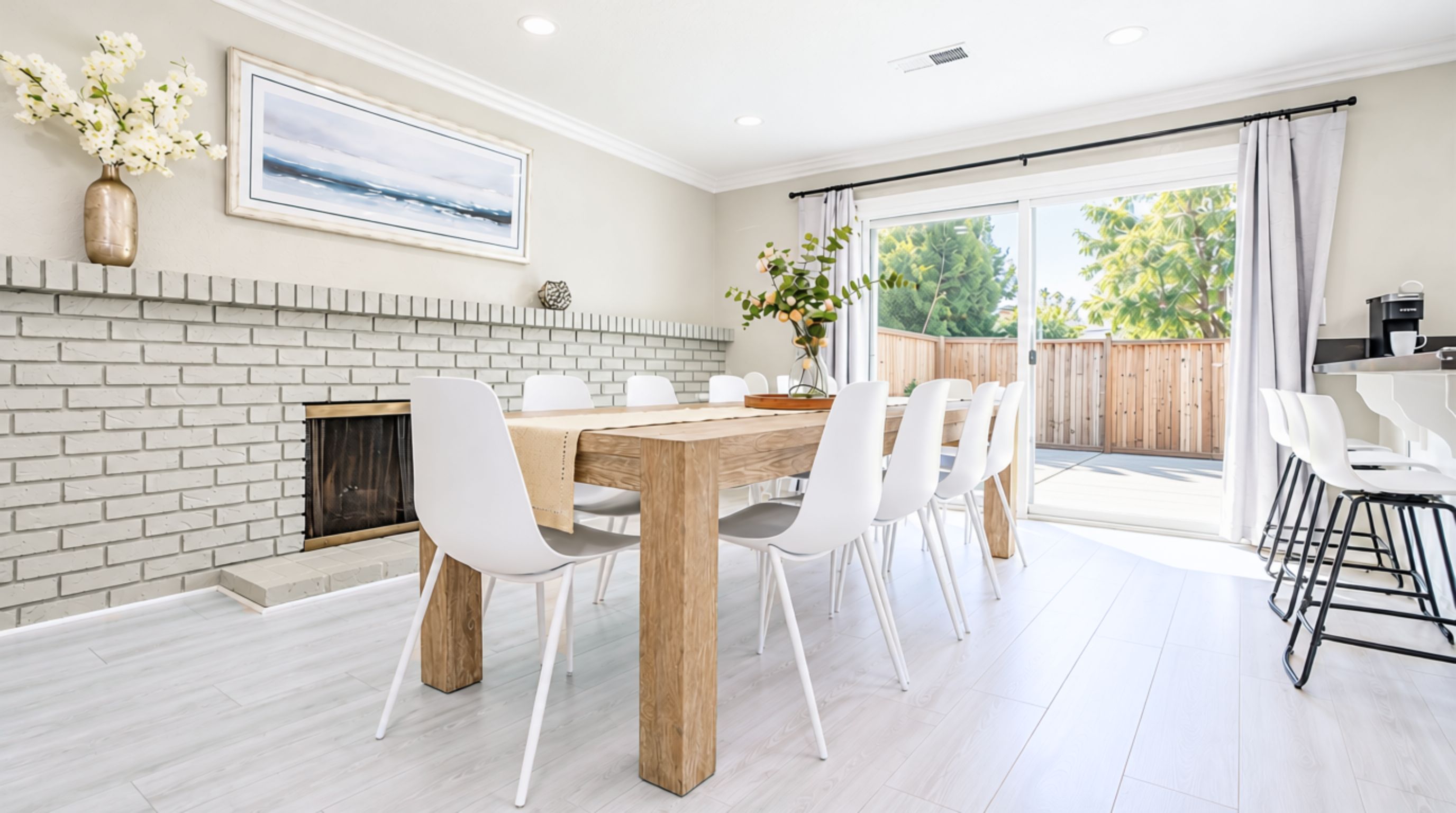 Un coin repas avec une cheminée en briques, des chaises blanches et une table en bois.