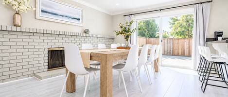 A dining area with a brick fireplace, white chairs, and a wooden table.