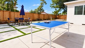 An outdoor ping pong table with a blue playing surface, surrounded by a concrete patio with grass edging. - Modern Spacious 5BR Retreat - Games & Large Yard (San Jose)