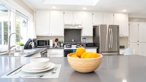 A modern kitchen with white cabinetry, stainless steel appliances, and a central island with a bowl of fruit. - Modern Spacious 5BR Retreat - Games & Large Yard (San Jose)