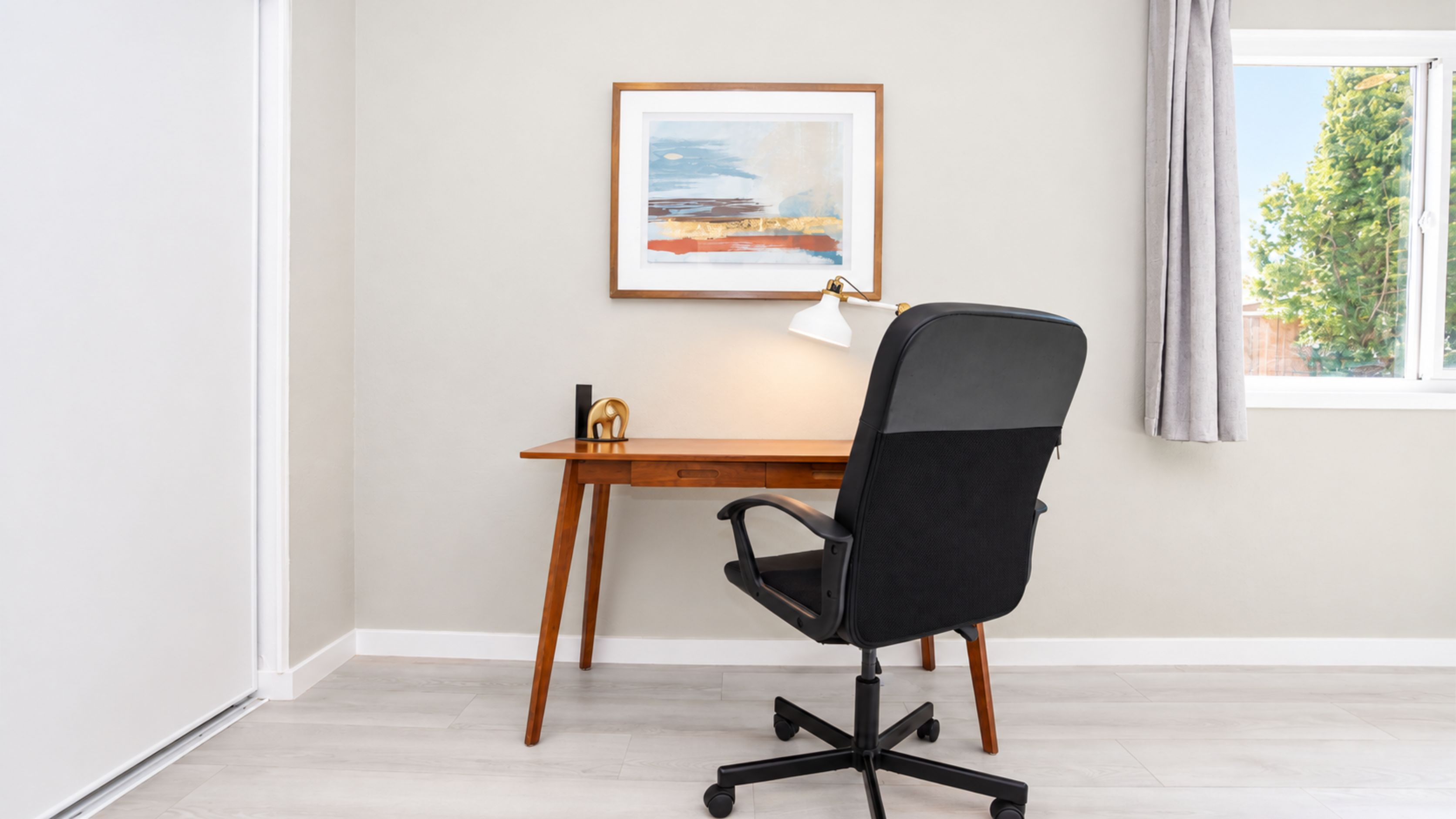 A workspace with a desk, chair, lamp, and a framed picture on the wall.