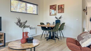 A modern living room with a round wooden coffee table, a dining table with chairs, a TV, and artwork on the walls. - Stunning home in Hellendoorn with WiFi (Hellendoorn)