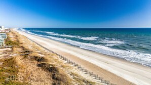 Ein Strand mit einer Holzstege, der zu einem Gebäude mit einem Balkon führt.