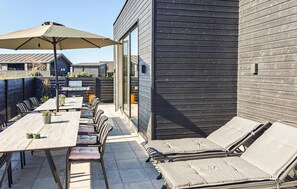 An outdoor patio with a table and chairs, a grill, and a lounge area with cushions.