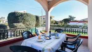 A covered outdoor dining area with a table set for two, surrounded by chairs, and a view of the neighborhood.