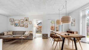 A modern living room with a wooden dining table, a sofa, and a view of the outdoors. - 3 bedroom lovely home in Ebeltoft (Ebeltoft)