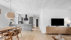 A modern kitchen with a central island, a dining area with a wooden table and chairs, and a living area with a TV and lamp. - 3 bedroom lovely home in Ebeltoft (Ebeltoft)