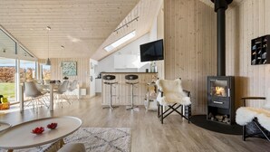 A spacious living area with a high ceiling, wooden walls, a fireplace, and a kitchen area with bar stools.