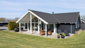 A modern house with a covered patio, a lawn, and a black exterior.
