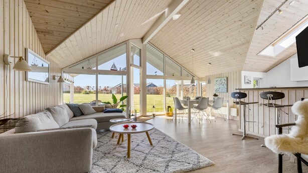 A spacious living area with a high ceiling, large windows, and a view of a grassy field.