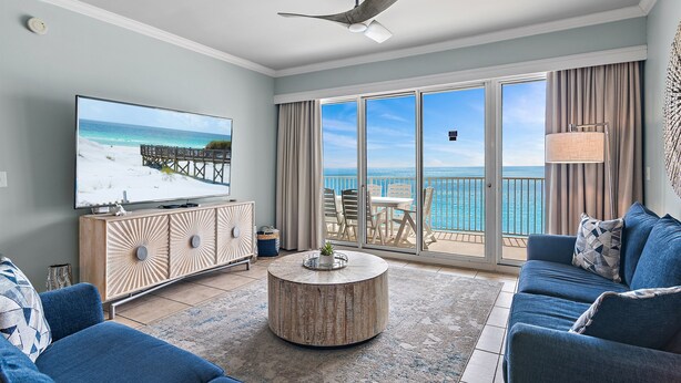A modern living room with a large TV, a round coffee table, and a sofa. The room has a view of the ocean through large sliding glass doors. - Beach Front Unit - Tops'l Resort - Free Pickleball - Tides 1304 (Miramar Beach)