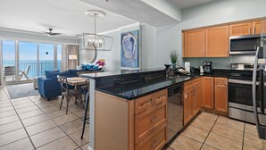 A modern kitchen with wooden cabinets, a black countertop, and stainless steel appliances. - Beach Front Unit - Tops'l Resort - Free Pickleball - Tides 1304 (Miramar Beach)