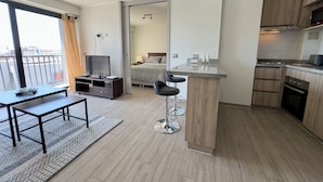 Una habitación de hotel moderna con balcón, comedor, kitchenette y dormitorio independiente.