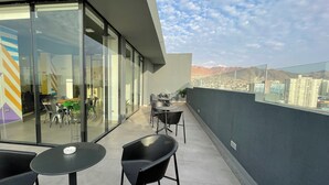 Een modern balkon met glazen wanden, een eethoek met stoelen en tafels, en een stadsgezicht.
