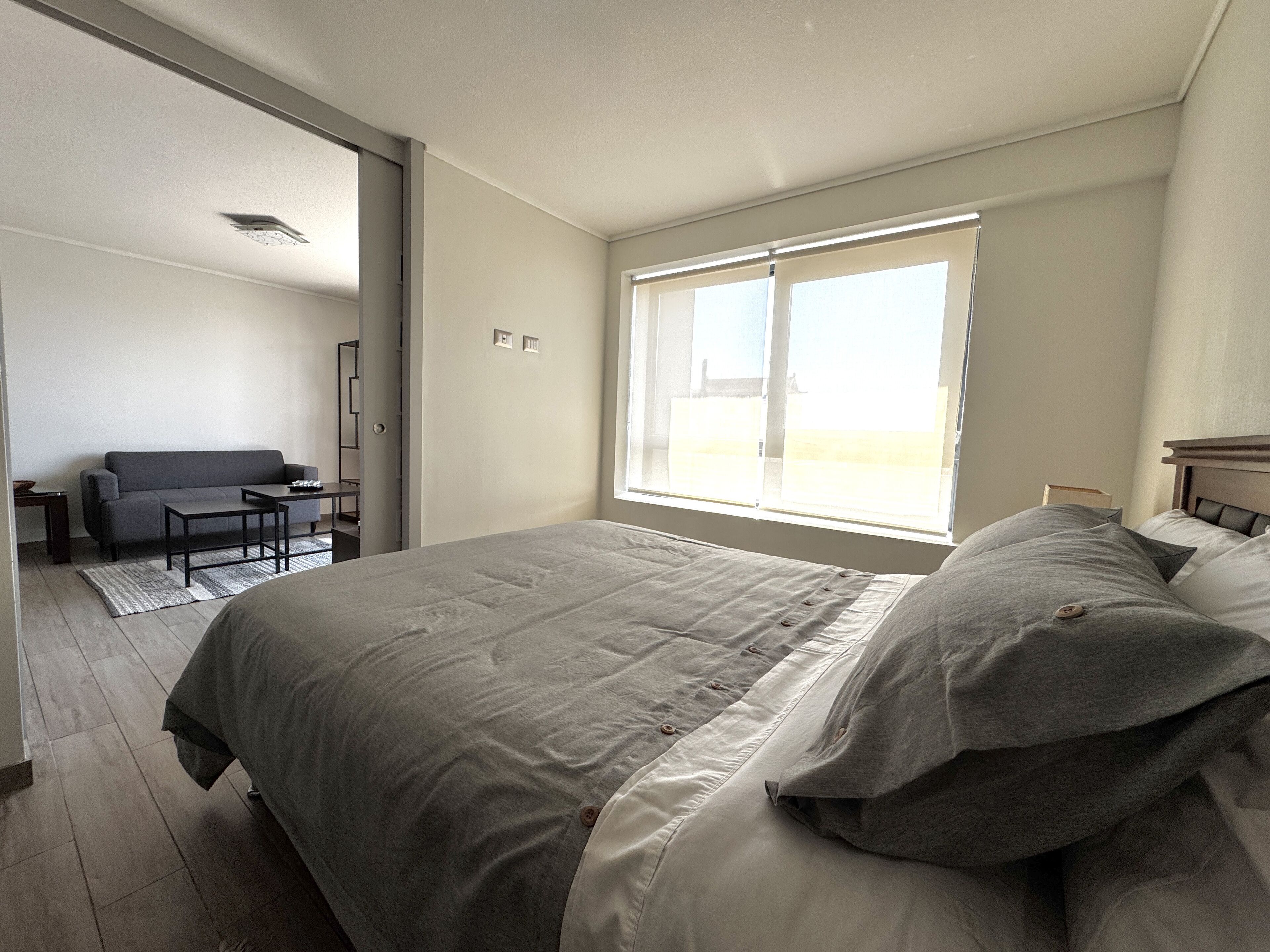 Un dormitorio moderno con una cama grande, un escritorio pequeño y vistas al exterior a través de una ventana.