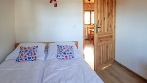 Een slaapkamer met een houten deur, een bed met witte beddengoed en bloemenkussens, en een kleine decoratie aan de muur.