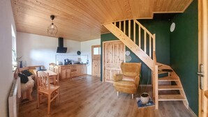 Een ruime woonkamer met een houten trap, een eettafel en een comfortabele fauteuil.