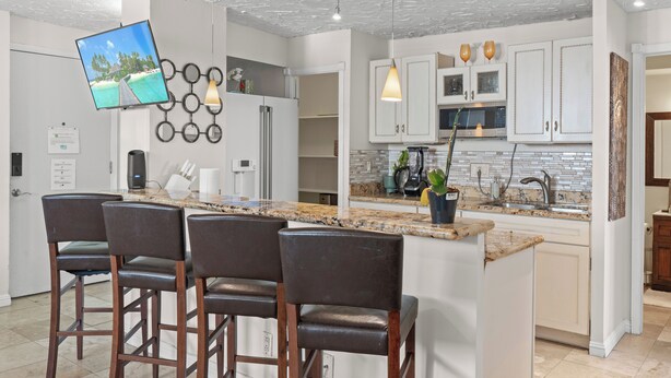 A modern kitchen with a central island, bar stools, and a flat-screen TV mounted on the wall. - Ocean View Mid Waikiki 1 Block to the Beach (Honolulu)