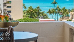 A balcony with a view of the ocean, palm trees, and a building in the background. - Ocean View Mid Waikiki 1 Block to the Beach (Honolulu)