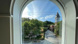 Una veduta attraverso una finestra mostra una strada con un attraversamento pedonale, una chiesa con campanile e case residenziali.