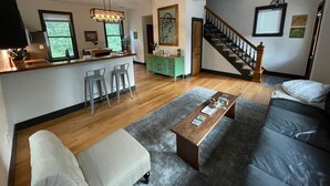 Un'ampia zona giorno con una scala in legno, una cucina con bancone e un'ampia finestra che fa entrare luce naturale.