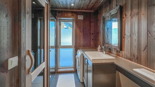 A wooden cabin interior with a bathroom featuring a sink, mirror, and a view of the outside. - Cozy home in Sjusjøen with sauna (Sjusjøen)