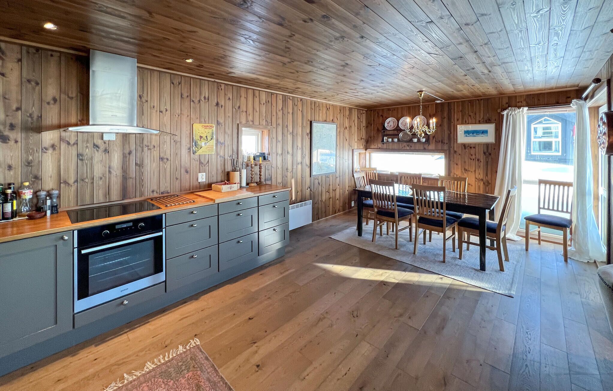 Interior de madera con cocina y comedor, que incluye una isla central, armarios empotrados y una araña.