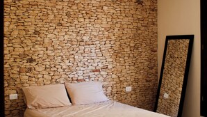 Une chambre avec un mur en pierre, un lit avec un cadre en bois, un ventilateur de plafond et un grand miroir.