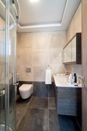 A modern bathroom with a glass shower enclosure, a toilet, a sink with a mirror, and a towel rack. - Seaside Private Beach Paradise (Kos)