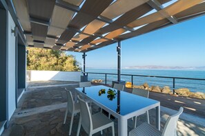A covered outdoor dining area with a table and chairs, overlooking a body of water and a distant coastline. - Seaside Private Beach Paradise (Kos)