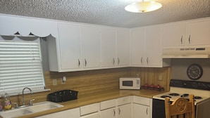 A kitchen with white cabinets, a microwave, a stove, and a wooden floor. - Cozy 2-bedroom cabin with WiFi, AC in charming Murfreesboro on Lake Greeson. (Murfreesboro)