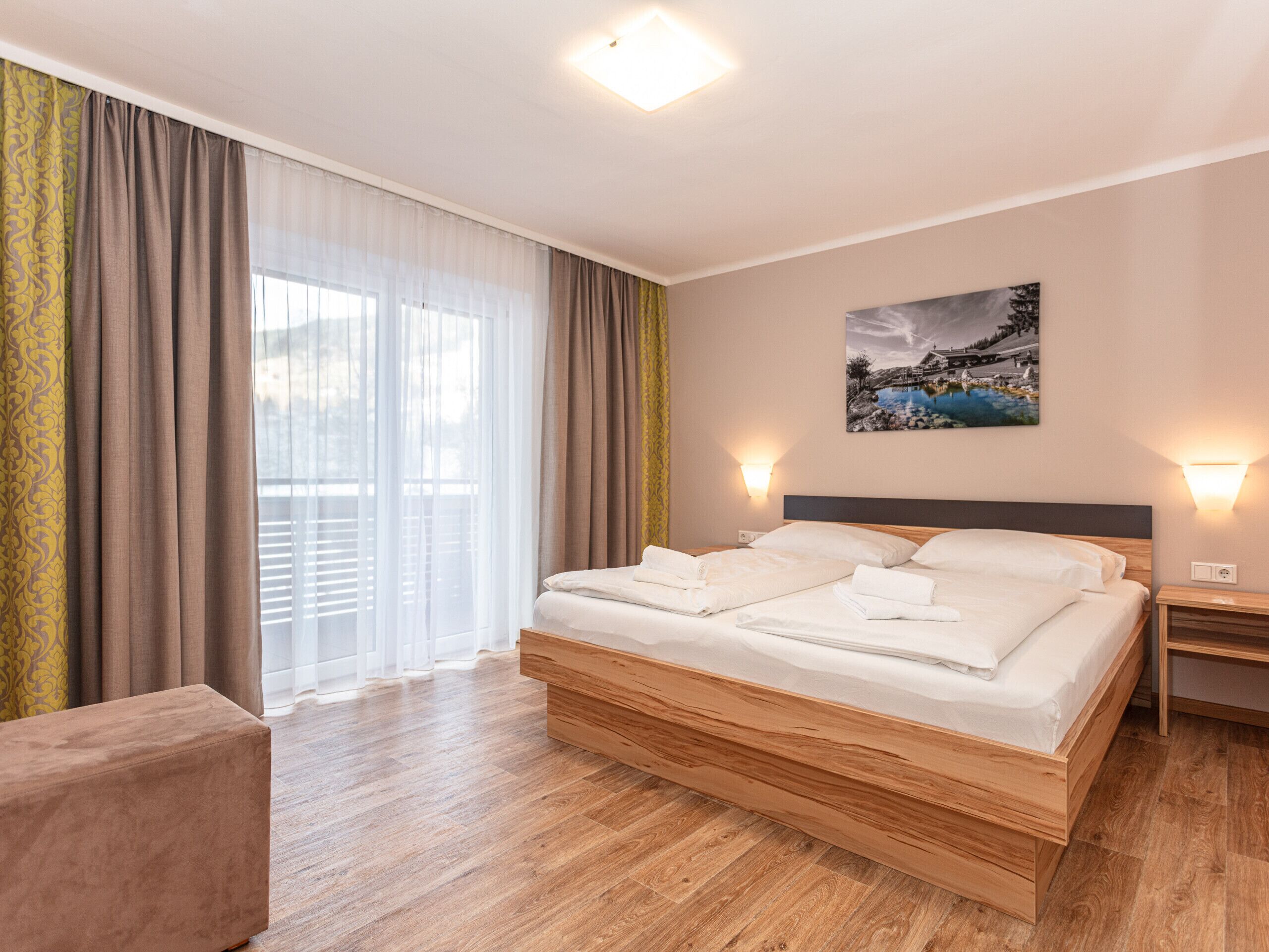 A hotel room with a large bed, wooden headboard, and a painting on the wall.