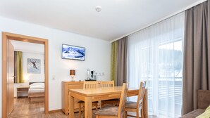 A hotel room with a wooden dining table, chairs, a bed, a TV, and a window with curtains.